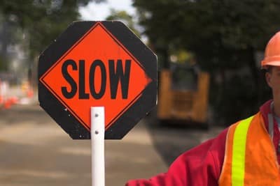 Image of a man holding a stop sign in the middle of the road as part of traffic control at a construction jobsite.
